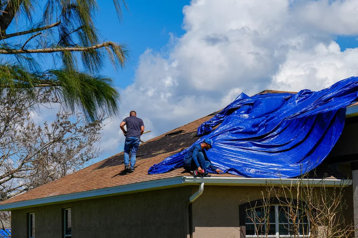 Workers placing a protective tarp over a damaged roof